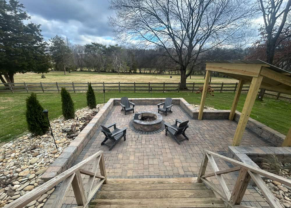Backyard paver patio with built-in fire pit, Adirondack chairs, stone retaining walls, and decorative rock drainage